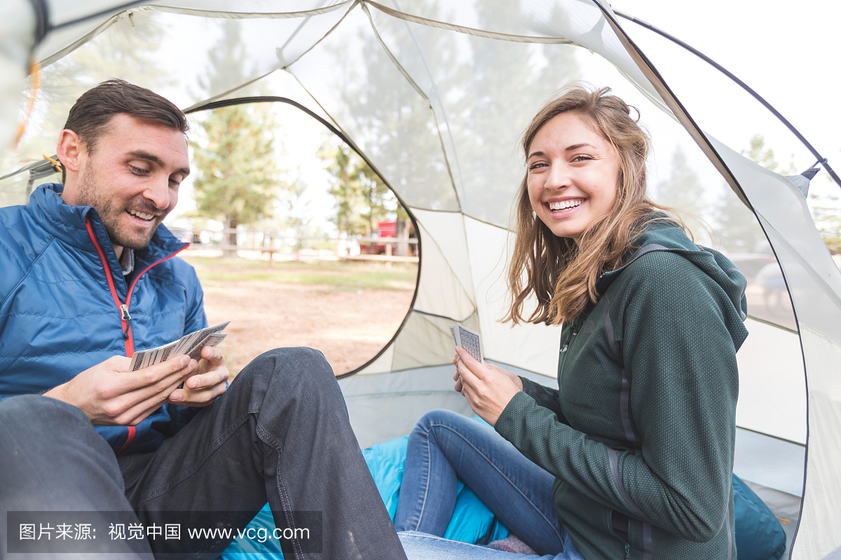 Millennial couple play cards in their tent on a ca Millennial couple play cards in their tent on a ca